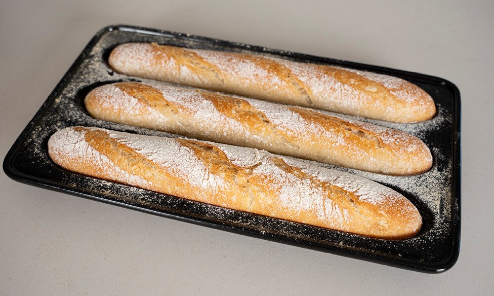 Drei frisch gebackene Baguettes auf einem bemehlten Blech.