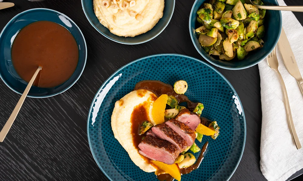 Gebratenes Entenbrustfilet mit Soße auf Polenta mit Rosenkohl und Orangenscheiben.