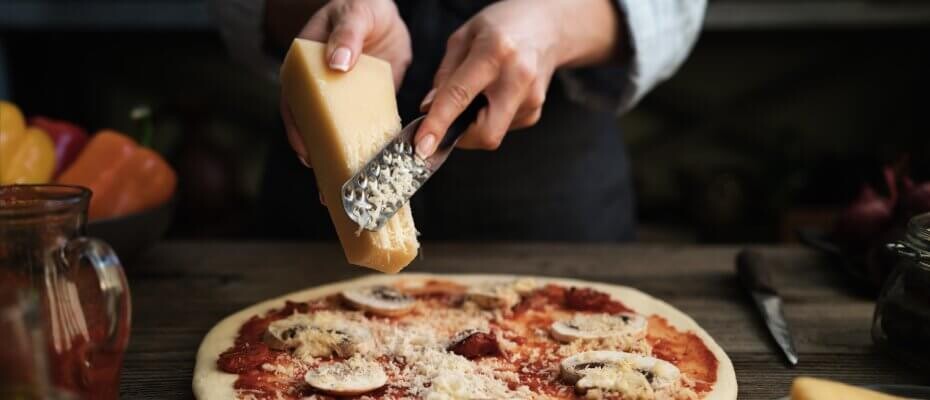 Frau reibt Käse mit einer Käsereibe auf Pizza
