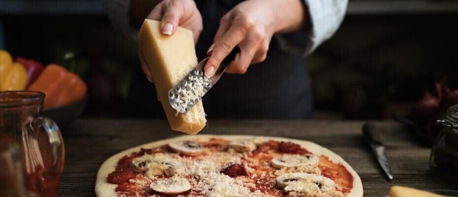 Frau reibt Käse mit einer Käsereibe auf Pizza