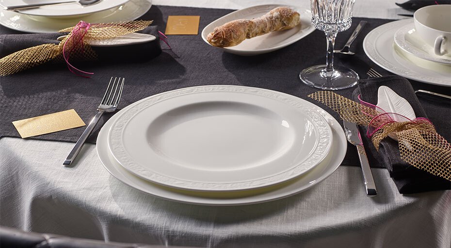 Elegante Tischgedeck mit weißem Teller der Serie White Pearl von Villeroy &amp; Boch, Besteck, Glas und serviertem Baguette auf dunkler Tischdecke.