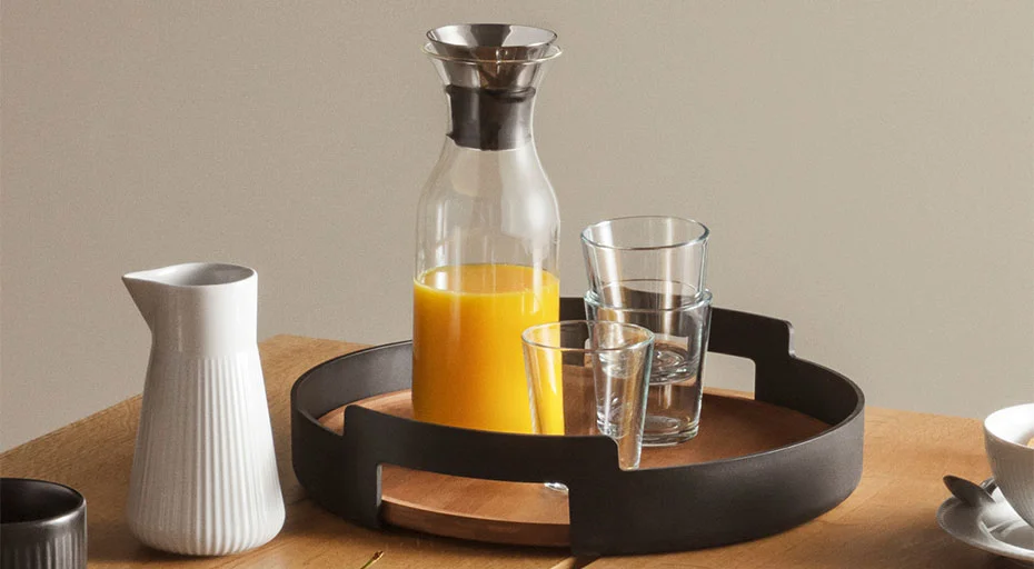 Tablett mit Gläsern, Karaffe von Eva Solo mit Orangensaft und Krug auf Holztisch arrangiert.