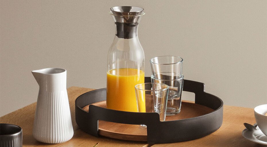 Tablett mit Gläsern, Karaffe von Eva Solo mit Orangensaft und Krug auf Holztisch arrangiert.