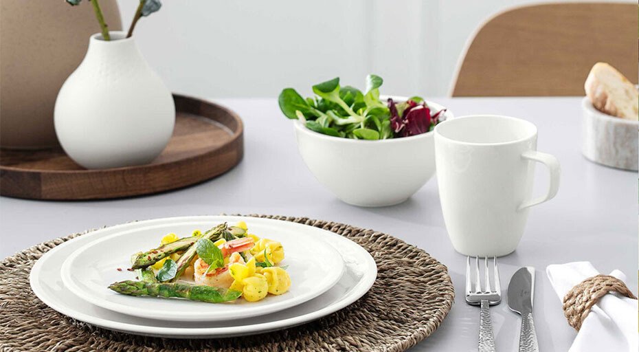 Ein Teller der Serie Artesano Original von Villeroy &amp; Boch mit grünem Spargel und Kartoffeln auf einem Tisch, daneben ein Salat in einer Schale und ein weißer Becher.