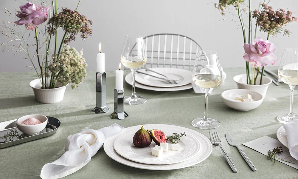 Eleganter Tisch mit weißem Geschirr der Serie Cellini von Villeroy &amp; Boch, dekoriert mit Feige und Käse, umgeben von Blumen, Kerzen und Weingläsern.
