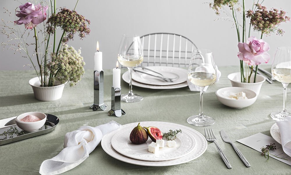 Eleganter Tisch mit weißem Geschirr der Serie Cellini von Villeroy &amp; Boch, dekoriert mit Feige und Käse, umgeben von Blumen, Kerzen und Weingläsern.