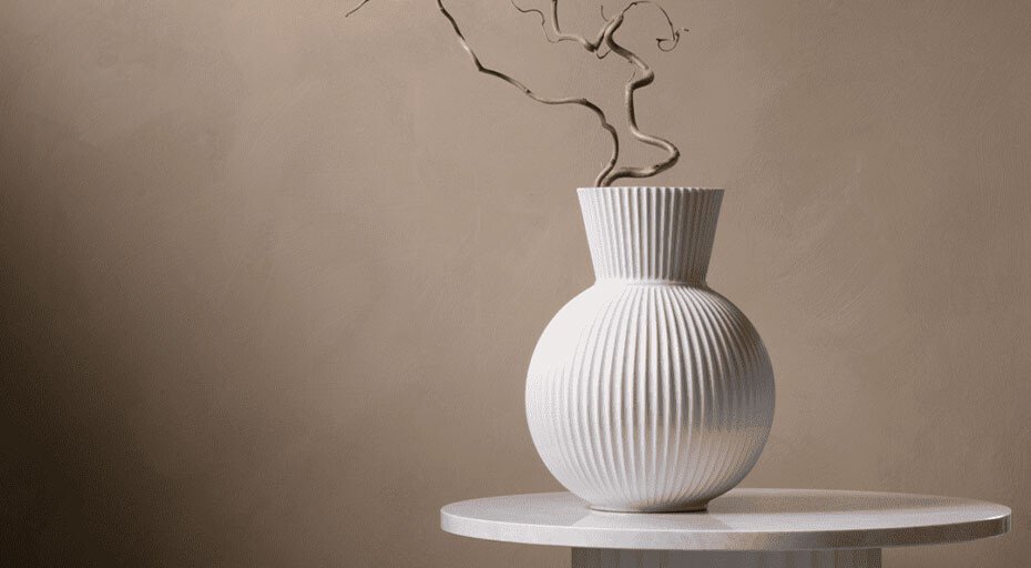 Weiße, geriffelte Vase von Lyngby mit trockenen Zweigen auf rundem Tisch vor beiger Wand.