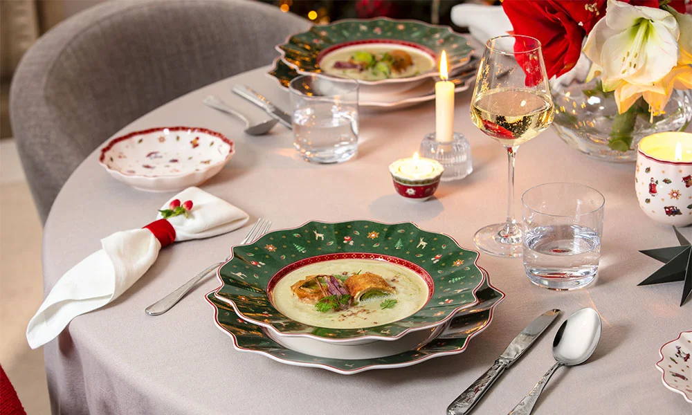 Festlich gedeckter Tisch mit Suppentellern auf Weihnachtsporzellan der Serie Toy's Delight von Villeroy &amp; Boch, Weingläsern und Kerzenlicht.