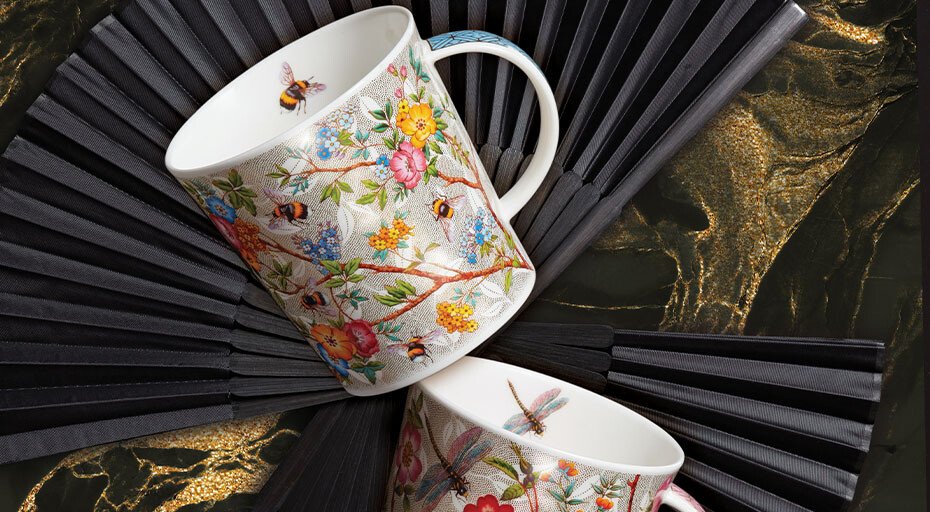 Zwei Tassen mit floralen und Insekten-Motiven von Dunoon auf Fächern liegend vor marmoriertem Hintergrund.