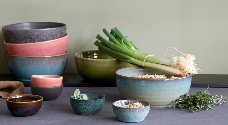 Poke Bowls von ASA in verschiedenen Größen und Farben, gefüllt mit Zutaten wie Lauch und Kräutern, auf einem grauen Untergrund.