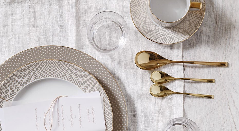 Porzellan-Service der Serie Francis Carreau Beige von Rosenthal mit goldenen Löffeln und Glas auf weißer Tischdecke arrangiert.
