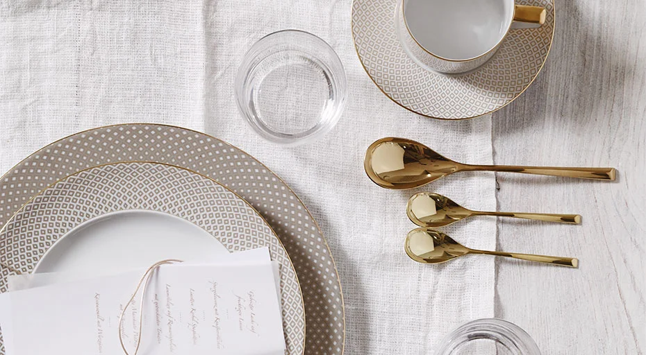 Porzellan-Service der Serie Francis Carreau Beige von Rosenthal mit goldenen Löffeln und Glas auf weißer Tischdecke arrangiert.