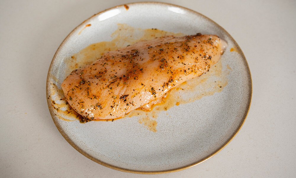 Ein mariniertes Hühnerbrustfilet liegt auf einem Teller, mariniert mit Kräutern und Gewürzen.