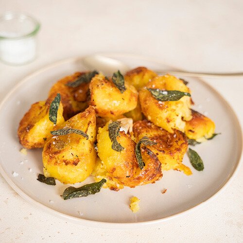 Geröstete Kartoffeln mit knuspriger Kruste, garniert mit Salbeiblättern und Meersalz, auf einem Teller serviert.