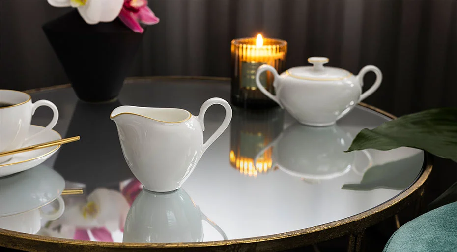 Villeroy &amp; Boch Milchkännchen auf einem gedeckten Tisch mit Porzellangeschirr, einer brennenden Kerze und einer Orchidee im Hintergrund.