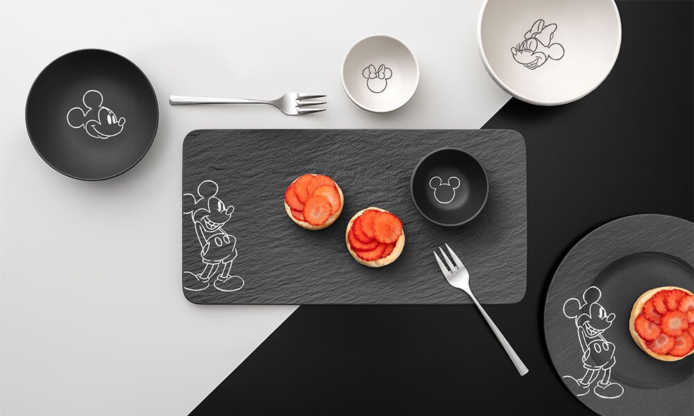 Teller- und Schüsselset der Serie Villeroy &amp; Boch Manufacture Rock – Mickey Mouse mit Mickey-Maus-Motiven, schwarze und weiße Designs, serviert mit Gebäck und Erdbeeren auf Schieferplatte.
