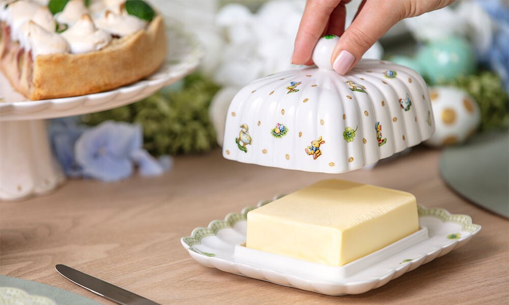 Butterdose der Serie Easter Delight von Villeroy &amp; Boch mit geöffneter Haube, zeigt ein Butterstück auf einem dekorativen Tisch.