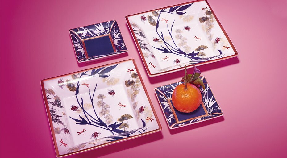 Porzellangeschirr der Serie Heritage von Rosenthal mit botanischen Mustern, arrangiert auf rosa Hintergrund. Eine Mandarine auf einem kleinen Teller.