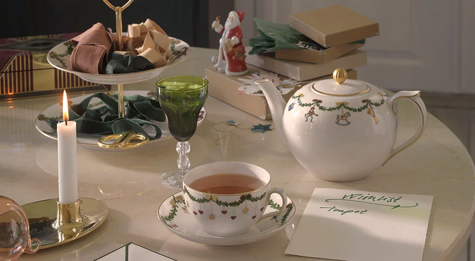 Stilvoll gedeckter Tisch mit Teeservice der Serie Star Fluted Christmas von Royal Copenhagen, Kerze, gefülltem Glas und Geschenken. Weihnachtliche Dekoration rundet das Ambiente ab.