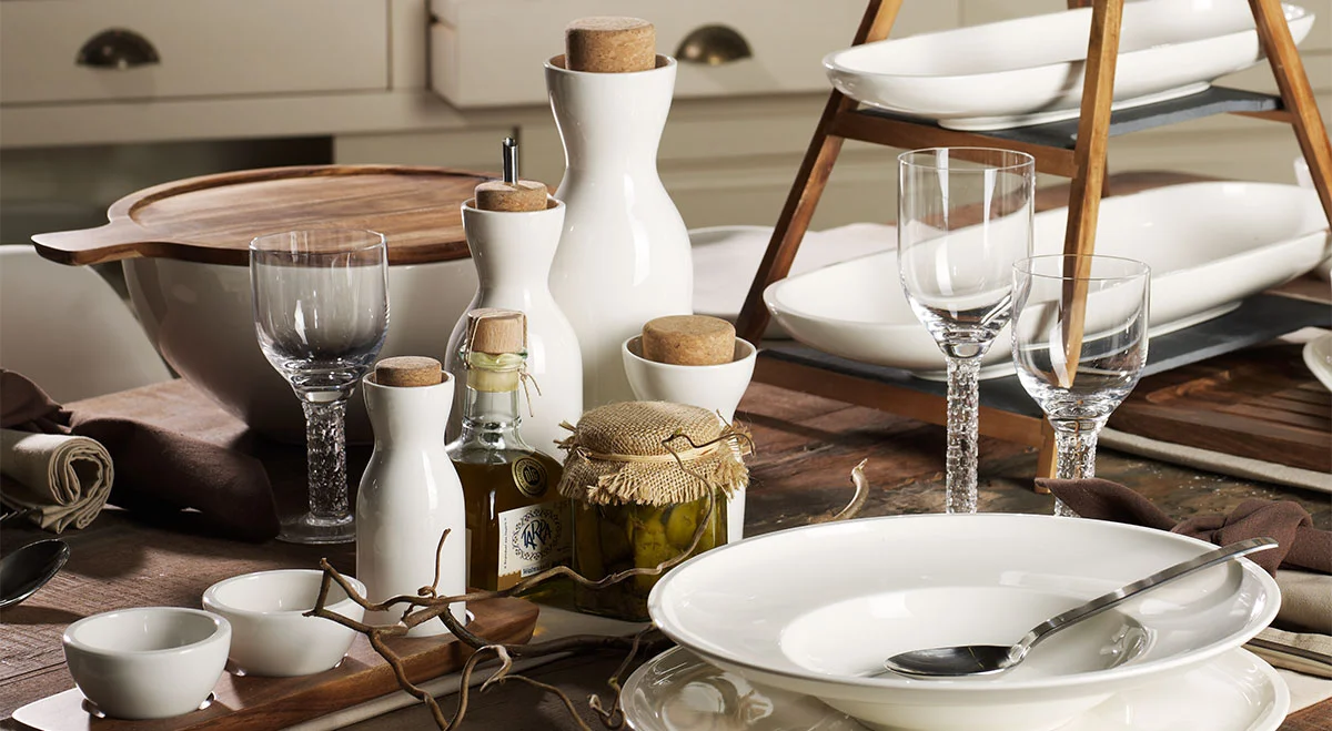 Tisch mit Geschirr der Serie Artesano von Villeroy &amp; Boch, Besteck, Gläsern, Gewürzen und einer Etagere, arrangiert für ein elegantes Essen in rustikaler Umgebung.