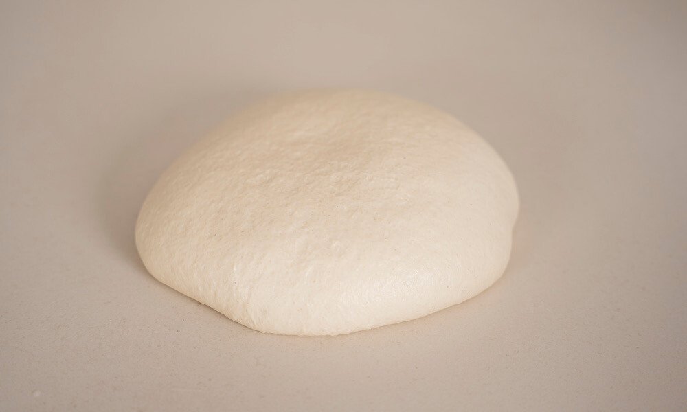 Hefeteigkugel auf einer glatten, hellen Oberfläche, bereit zum Gehenlassen oder Weiterverarbeiten.