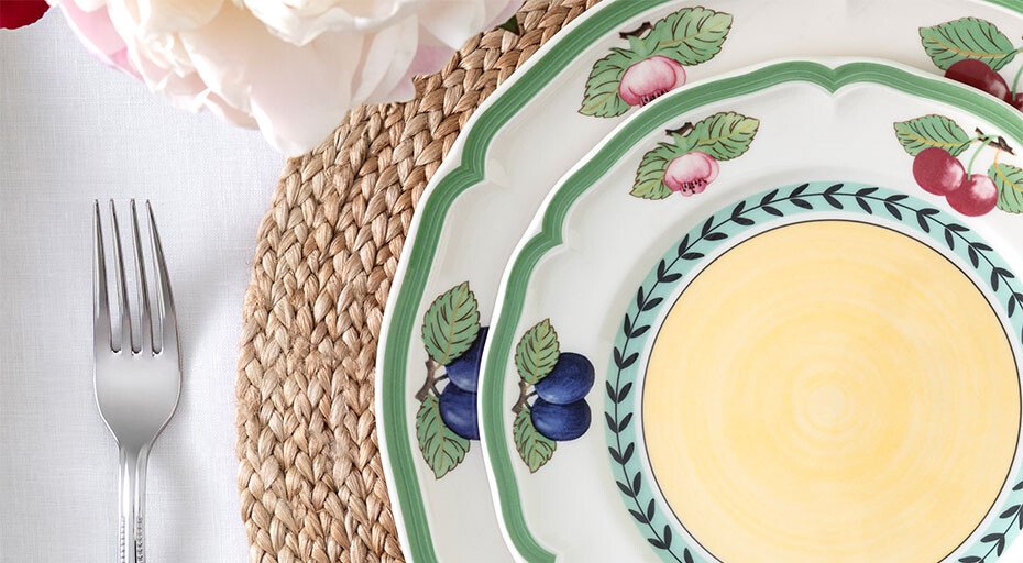 Zwei Teller der Serie French Garden von Villeroy &amp; Boch mit Früchte- und Blumenmuster auf rundem, gewebtem Tischset. Daneben eine Gabel.