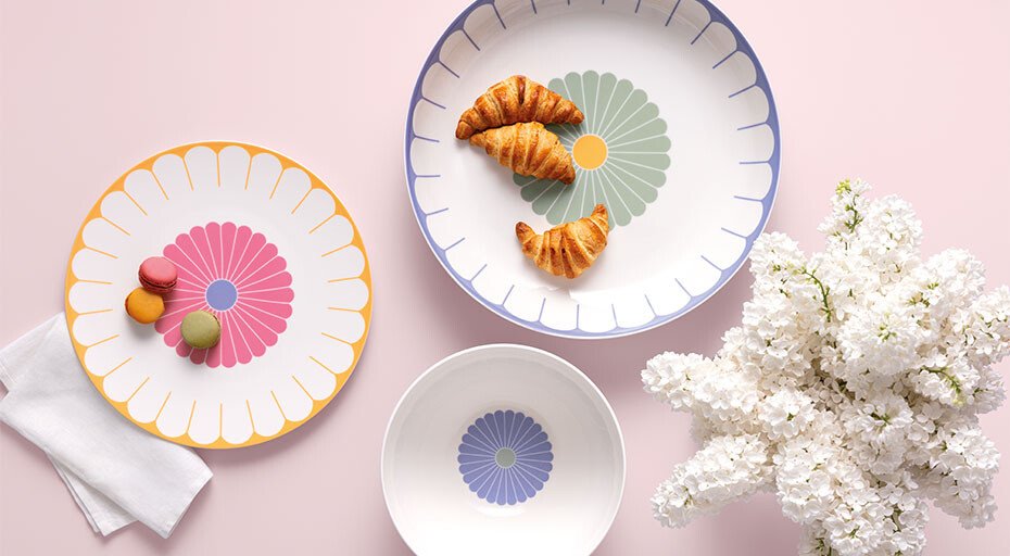 Drei Teller der Serie Fleur von Villeroy &amp; Boch mit Blumenmuster, serviert mit Croissants und Macarons, daneben ein Blumenstrauß auf rosa Hintergrund.