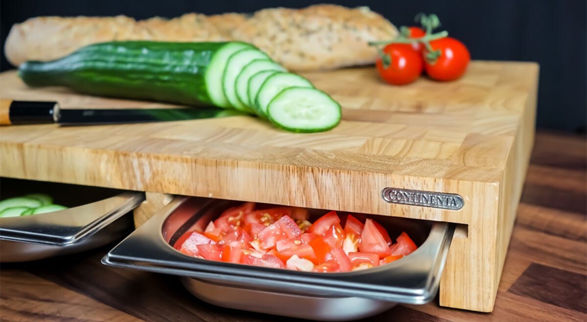 Schneidebrett von Continenta mit Schubladen, darauf geschnittene Gurken und ganze Tomaten; Brot im Hintergrund.