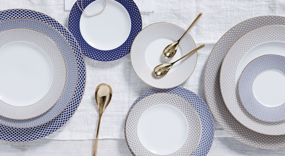 Porzellangeschirr der Serie Francis Carreau Bleu von Rosenthal mit blauen und silbernen Mustern, arrangiert auf weißer Tischdecke, goldene Löffel als Akzent.