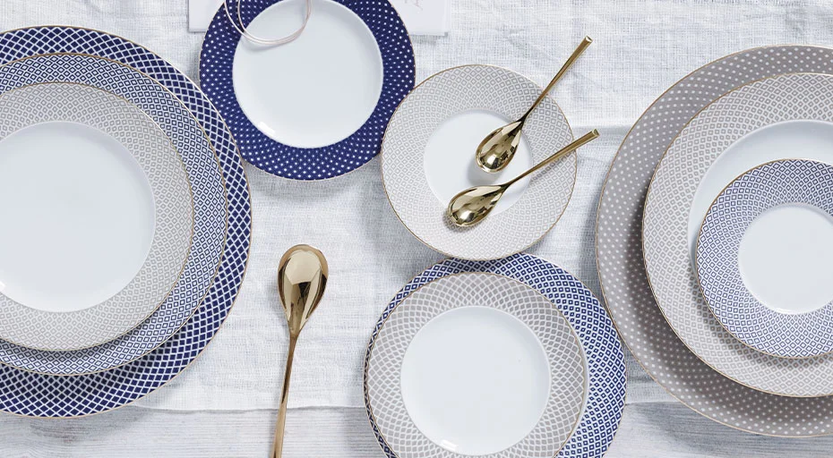 Porzellangeschirr der Serie Francis Carreau Bleu von Rosenthal mit blauen und silbernen Mustern, arrangiert auf weißer Tischdecke, goldene Löffel als Akzent.