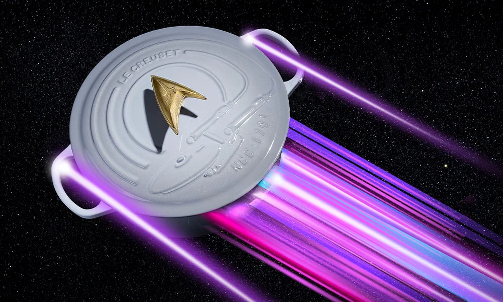 Grauer Le-Creuset-Star-Trek-Bräter mit goldenem Knauf und lila Lichtstrahlen auf Weltall Hintergrund.