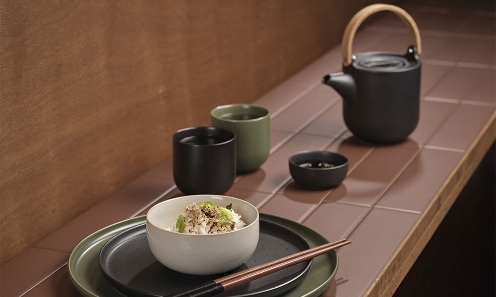 Japanisches Teeservice der Serie Coppa Kuro von ASA mit schwarzer Kanne, Tassen und Schalen auf brauner Fliesenfläche, serviert mit Reisgericht.