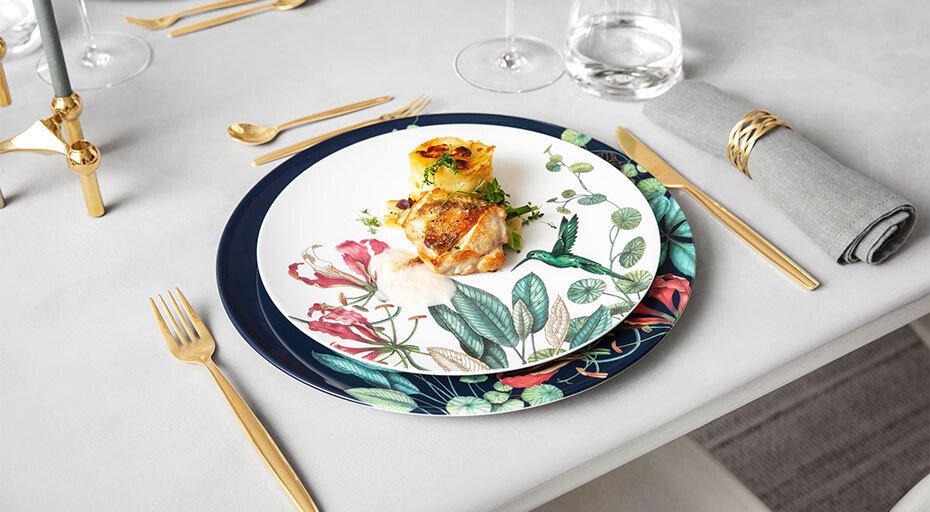 Elegantes Gedeck mit goldfarbenem Besteck, floralem Porzellanteller der Serie Avarua von Villeroy &amp; Boch und kunstvoll angerichtetem Fischgericht.