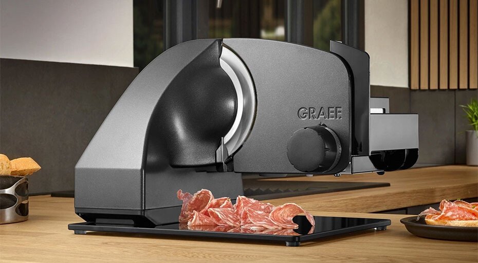 Elektrische Aufschnittmaschine von Graef auf Küchenarbeitsplatte, schneidet dünne Scheiben von rohem Fleisch.