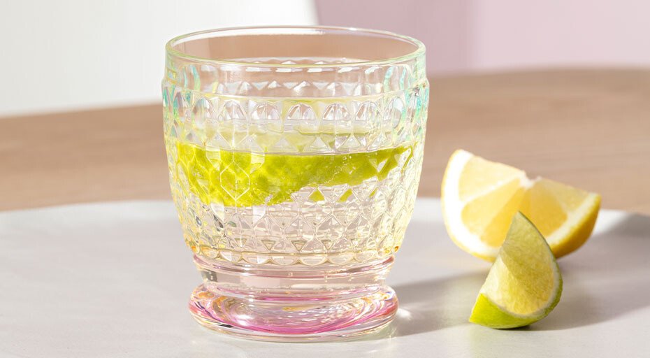 Ein Glas der Serie Boston Pearl von Villeroy &amp; Boch mit geometrischem Muster, gefüllt mit Wasser und einer Limettenscheibe. Daneben Limetten- und Zitronenstücke.