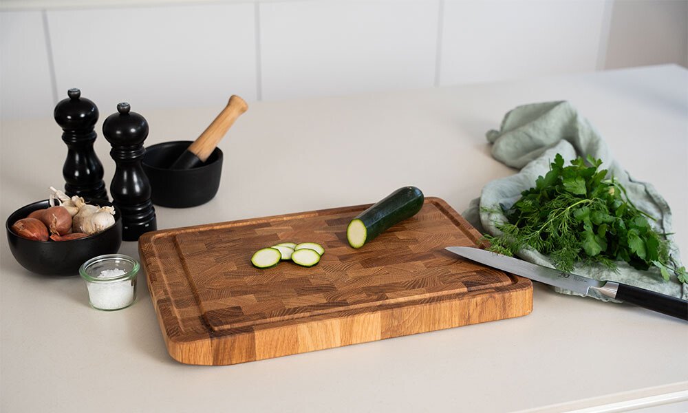 Holzschneidebrett von Continenta mit geschnittener Zucchini, Kräutern, Messer, Gewürzmühlen und Mörser auf einer Küchenarbeitsfläche.
