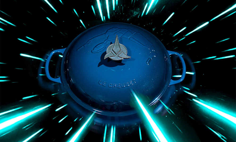Blauer Le Creuset-Topf mit klingonischem Symbol, umgeben von leuchtenden Lichtstreifen auf schwarzem Hintergrund.