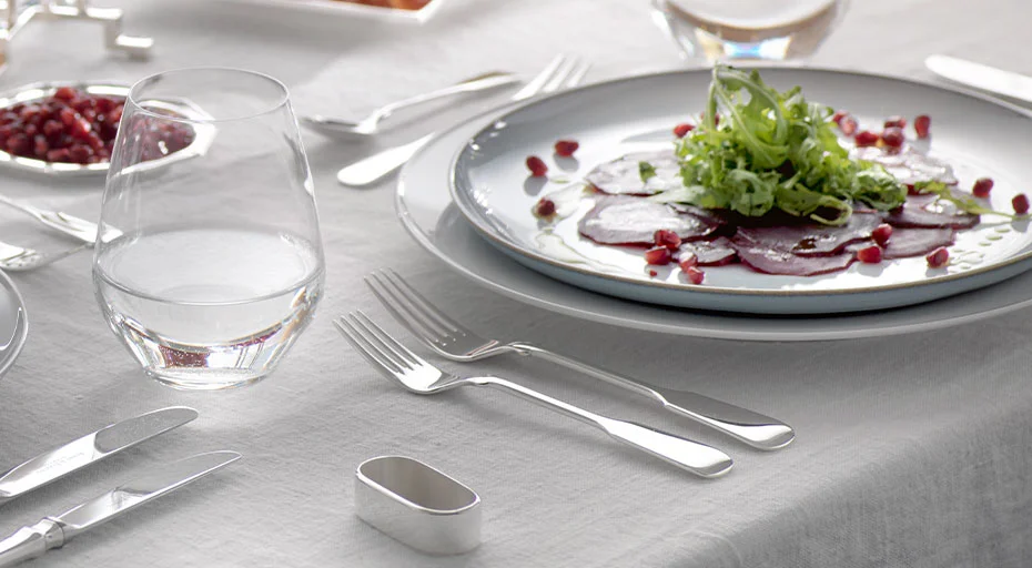 Gedeckter Tisch mit Besteck der Serie Spaten von Robbe &amp; Berking, Wasserglas und Teller mit Carpaccio und Salatgarnitur.