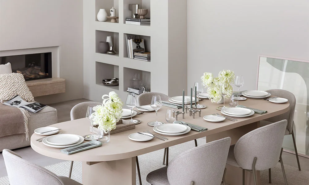 Eleganter Essbereich mit gedecktem Tisch, weißen Tellern der Serie Afina von Villeroy &amp; Boch und Blumenarrangements, umgeben von minimalistischer Inneneinrichtung.